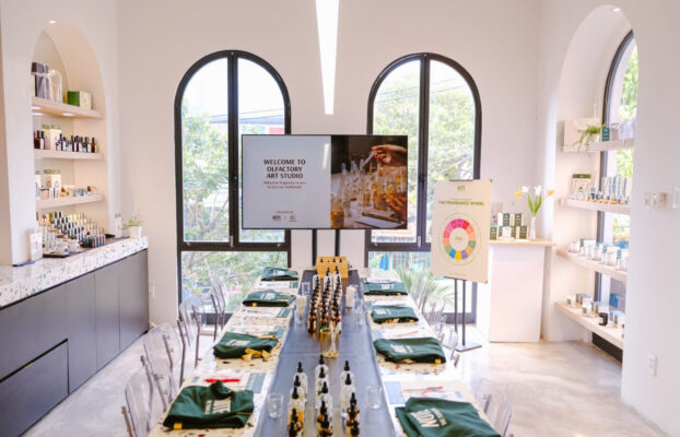 NOTE – The Scent Lab 34 Nguyen Duy Hieu - Workshop nước hoa tại Hà Nội và TP Hồ Chí Minh by NOTE Bright fragrance shop workshop space with a long table set for a class, surrounded by product shelves and large arched windows outside light streaming in.
